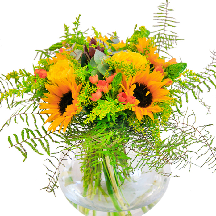 This exuberant floral arrangement mirrors the vibrant spontaneity of Greenwich life-its centerpiece: sunflowers, their immense golden heads beaming against a pure white backdrop, reminiscent of sunlight streaming down King William Walk. Nestled among them, smaller yellow flowers-solidago or mimosa perhaps-bubble up, their round clusters adding both texture and playful movement. A few gentle coral-orange blooms peek through, offering soft contrast and recalling the subtle hues found in Greenwich's springtime markets. The bouquet is threaded through with lush greenery, including feathery ferns unfurling with elegance and silvery eucalyptus lending a modern, crisp accent. Each stem is artfully displayed within a rounded, clear glass vase, revealing the vibrant tangle of fresh cut stems and the natural clarity of water. Designed with a discerning Greenwich eye, this arrangement feels both lively and serene, like a sunlit stroll through the Royal Observatory gardens. Whether as a cheerful centrepiece in a riverside flat or a thoughtful local delivery across SE10, the bouquet is a heartfelt expression of joy, invoking the warm welcomes and creative flairs of the Greenwich community.